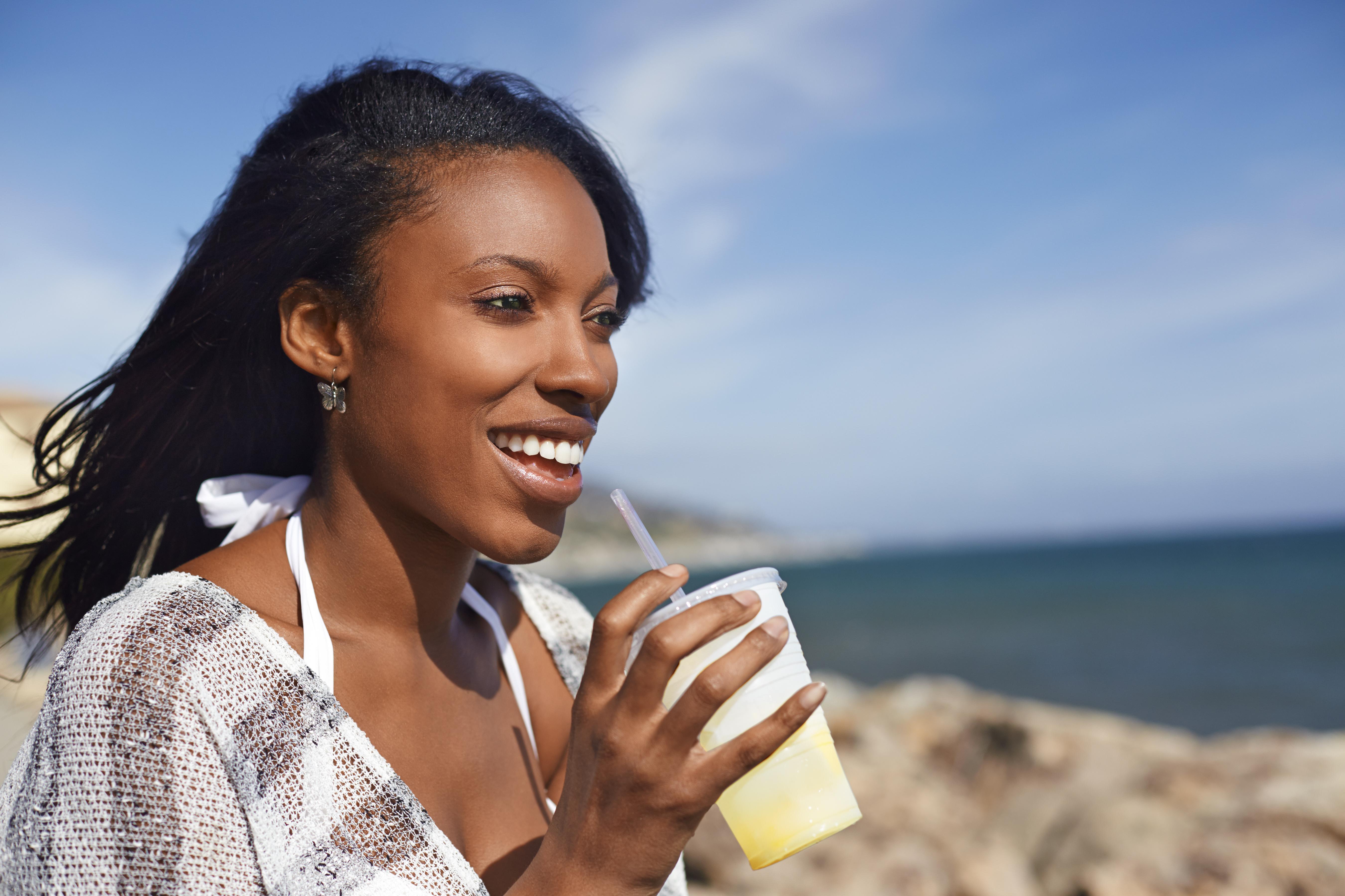 Young woman drinking fruit juice at beach, Malibu, California, USA