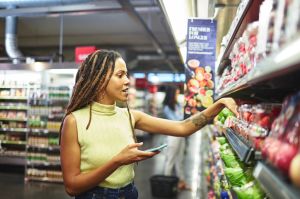 Woman with smart phone grocery shopping in supermarket