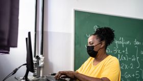 Mature teacher using a computer in the classroom - using a face mask