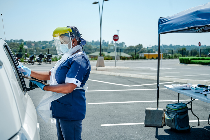 Shot of an unrecognizable nurse wearing a face shield and filling in Covid19 screening test forms at a car window
