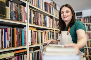 Portrait of a bookseller giving books to customer in a shelf