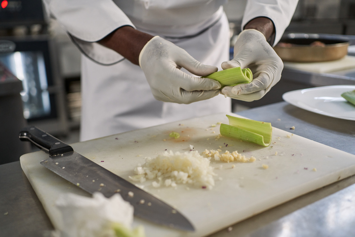 Dedicated male chef in uniform cutting onions for later preparation at the restaurant commercial kitchen