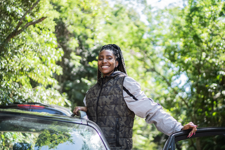 Portrait of a happy young woman getting out of car in a trail in the forest