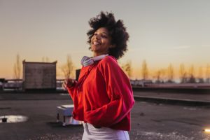 Smiling African young woman with headphones dancing on roof