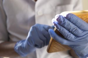 black healthcare worker wearing blue surgical gloves & white lab coat uses a smart phone