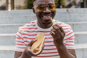 Portrait of a young African-American man is eating hot dog and smiling