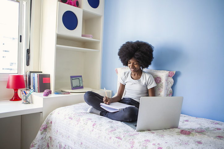 Teen girl studying with laptop in bed