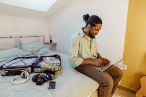 African-American man packing for a trip and checking mail on laptop