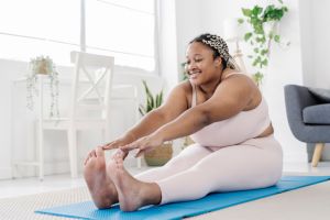 Young overweight African woman exercising at home while touching her hands with her feet. .
