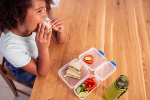 Elementary-age girl eating food from a lunch box at school.