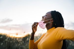 Happy teenage girl with eyes closed removing mask and inhaling in field during sunset