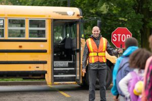 Smiling crossing guard helps students safely get on school bus
