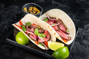 Mexican Steak Tacos with beef meat, cilantro, green sauce, jalapenos and onion. Black background. top view