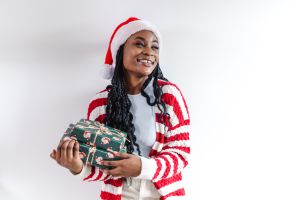 Young woman with a Santa hat holding a Christmas gift in front of the white wall