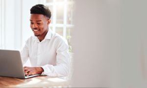 Internet, laptop and black man working in home office, happy freelance worker at desk. African startup businessman with smile, technology and online project for social media management company