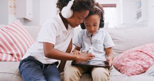 Headphones, tablet and children learning games in their home living room for education, digital development and holiday activity. Black family kids with audio, sound or music with a game app on sofa