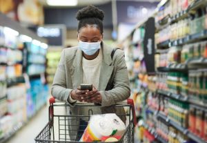Black woman, covid and phone in grocery store with product research, fintech shopping app or checking bank balance. Covid 19, face mask or supermarket customer on mobile technology for finance budget