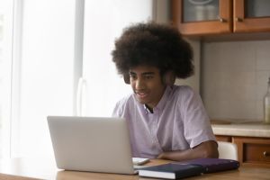 African student guy wear headphones use laptop studying at home