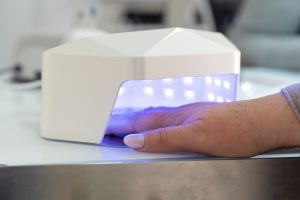 A hand of an older woman drying her nails in an ultraviolet lamp