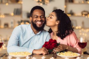 Young black woman kissing her man holding flowers