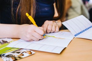 Girl is writing form with yellow pen in blue shirt on the wooden table,Romania