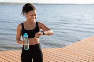 Athletic black woman drinking water, checking fitness bracelet