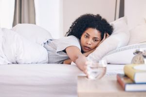 Health, black woman in bed and wake up with water, tired and fatigue with burnout, overworked and sleepy. African American female, girl and in bedroom with aqua, illness and wellness in the morning