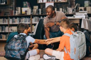 Elementary school teacher huddling with his students in a library