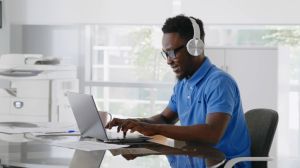 Cheerful african manager listening to music in headphones working on laptop