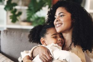 Black family, love and hug by girl and mother on a sofa, happy and relax in their home together. Mom, daughter and embrace on a couch, cheerful and content while sharing a sweet moment of bonding