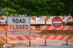 Yellow protective fence barrier at street construction site. Warning road sign about utility work