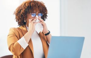 Sick, tissue and black woman with laptop in office with runny nose, allergy and virus infection at desk. Business, health problem and female worker with cold, fever and flu symptoms in workplace