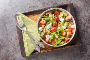 Homemade fresh salad of strawberries, avocado, bacon, lettuce, feta cheese close-up in a bowl. Horizontal top view