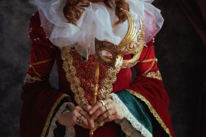 Closeup on medieval queen in red dress with venetian mask