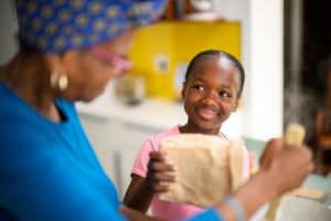 Happy girl smiles at grandmother while adding maize meal to the pot