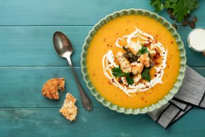 Pumpkin and carrot cream soup with herbs, seasonings and seeds in bowl on dark wooden background in rustic style. Thanksgiving traditional autumn pumpkin cream soup. Top view.