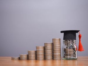 Glass bottle with graduation hat and stack of coins. The concept of saving money for education, student loan, scholarship, tuition fees in future