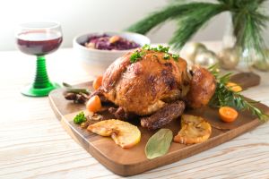 Roast chicken from the oven with fruits and herbs, served with red cabbage and wine on a wooden board, pine branches and Christmas decoration, holiday dinner with poultry, copy space