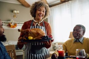 Happy mature woman serving Thanksgiving turkey to her family in dining room.