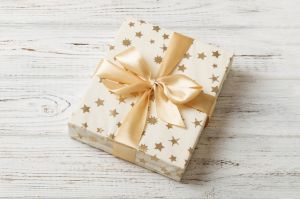 wrapped Christmas or other holiday handmade present in white paper with gold ribbon on colored background. Present box, decoration of gift on colored table, top view with copy space