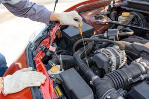 Closeup mechanic hand with protective glove checking the oil level of a car. Routine car maintenance for safe and efficient engine operation. Working atmosphere at car repair shop.