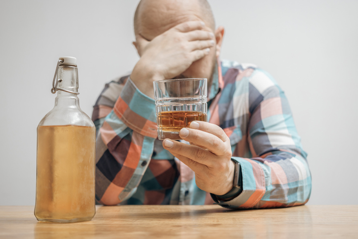 Addicted and drunk man at the table with a glass of alcohol drink, whiskey or brandy, alcoholism and bad habits concept