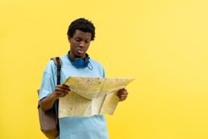 Confused African American Man With Map On Yellow Background, Travel, Direction, City, Exploration, Lost, Tourist, Vacation, Lifestyle