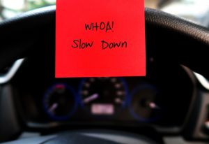 Red sticky note with text written WHAO! SLOW DOWN on the car steering wheel , to remind driver to drive slowly in limit speed for safety