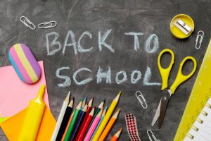Back to school concept with variety of office and school supplies on black chalkboard background.