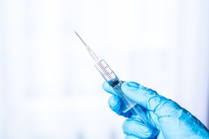 Human hand wearing medical gloves holds a syringe needle,Doctor hands with syringe on light background