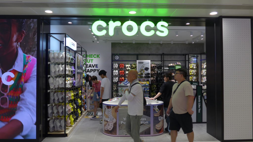 Pedestrians walk past the American footwear company Crocs...