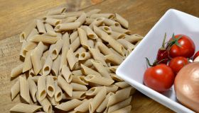 Durum wheat semolina penne pasta with cooking ingredients: onion, chilli pepper and tomatoes