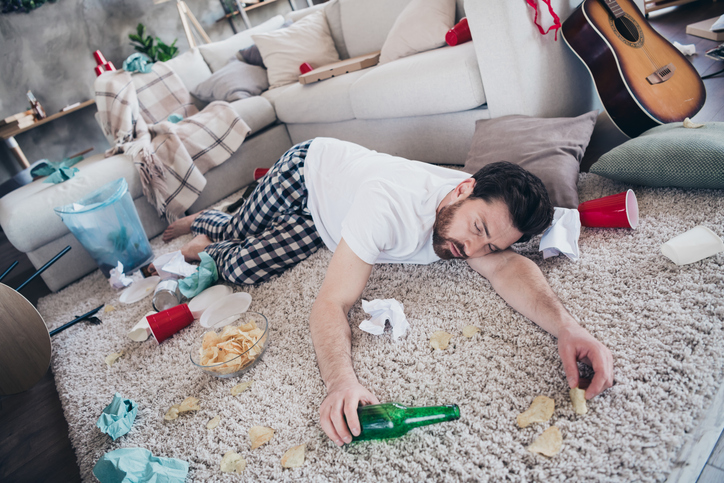 Full body photo of nice young man lying floor drunk wear pajama wake up after party messy modern interior flat indoors