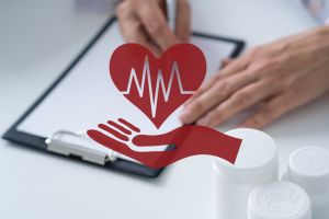Doctor's hands writing on medical tablet and red hand and heart icon on foreground, medical concept